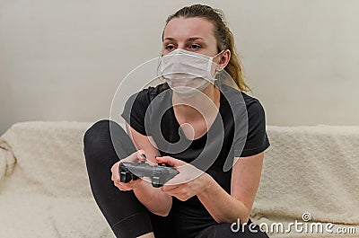 A young girl in a medical mask plays on a computer console using the joystick Stock Photo