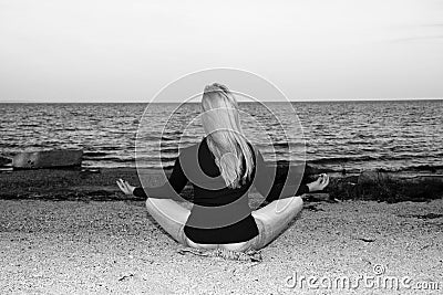 A young girl is meditating on the beach sitting on the shore Stock Photo