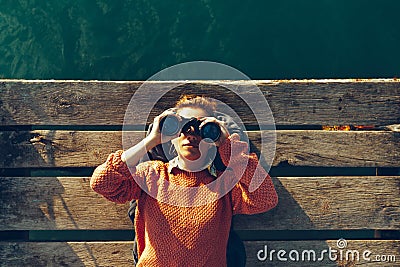 Young Girl Lies On A Pier Near The Sea And Looks Through Binoculars. Travel Search Journey Concept Stock Photo