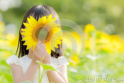 Young girl peeking behind sunflower in vibrant field with soft background, ideal for text overlay Stock Photo