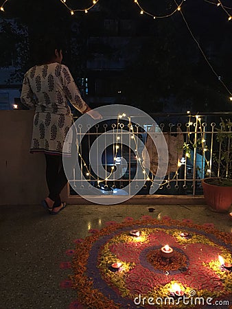 A young girl standing besides a brightly lit Rangoli during Diwali Stock Photo