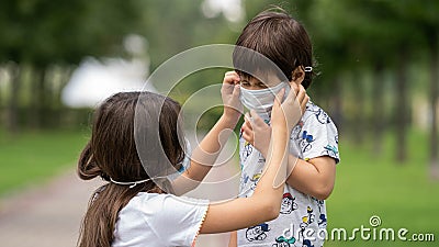 A young girl helps her brother to wear a face mask from the coronavirus covid19 Stock Photo