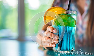 Young girl`s hand holding a glass with a blue lemonade cocktail with fruits Stock Photo