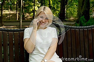 A young girl is sitting on a bench outside, smiling and talking on the phone Stock Photo