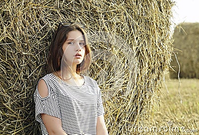 A young girl is sitting near a round stack of straw in a mown field of rye Stock Photo