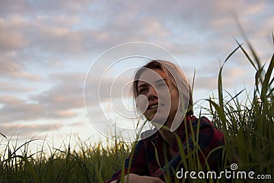 Young girl sitting in tall grass at sunset backlit Stock Photo