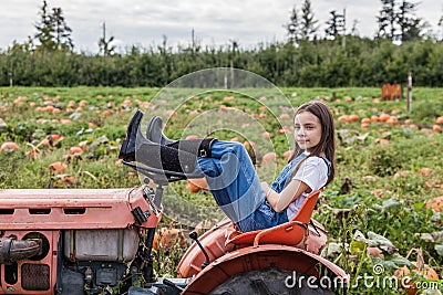 Young girl sitting on tractor in a green farm field Stock Photo