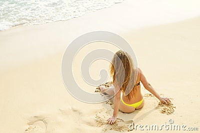 Young girl sitting on tropical beach turned wistfully looking at the sky. Summer woman background of the ocean and sand. Top view. Stock Photo