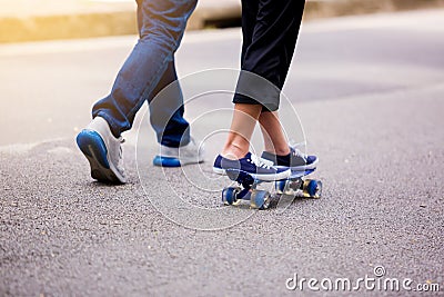 Young girl skateboarding with her dad running at park outdoor i Stock Photo