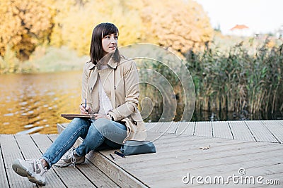 A young girl sketching near a lake in the autumn forest. Stock Photo