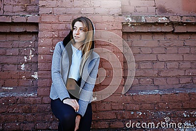 Young girl in a sportwear is exercising in front of the urban red brick wall. Phot was made on a sunny morning. Stock Photo