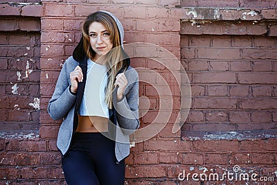 Young girl in a sportwear is exercising in front of the urban red brick wall. Phot was made on a sunny morning. Stock Photo