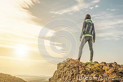 Young girl standing on top of a mountain and enjoying the view of the valley with the sunset. Stock Photo