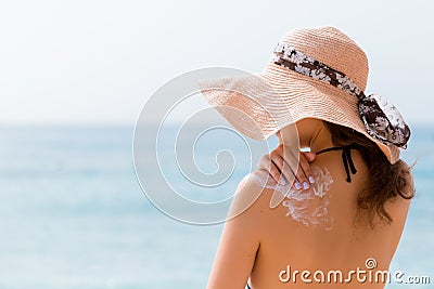 Young girl in straw hat is applying sunscreen on her back to protect her skin Stock Photo