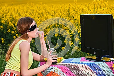 Young girl in sunglasses watches tv in the field dines on chips Stock Photo