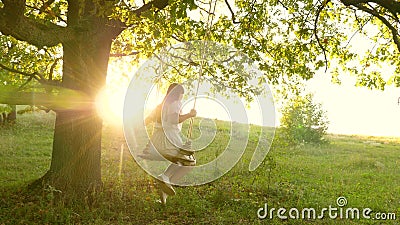Young girl swinging on a swing on an oak branch in sun. Dreams of flying. Happy childhood concept. Beautiful girl in a Stock Photo