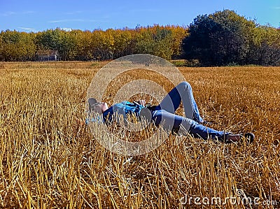 A young girl taking a break while working on a farm, laying down in a straw field looking up at the sky Stock Photo