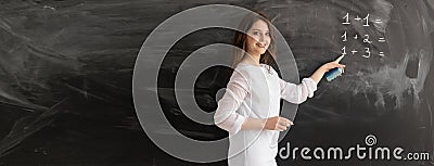 A young girl teacher or tutor is standing against the background of a chalk board with empty space for text. Math lesson Stock Photo
