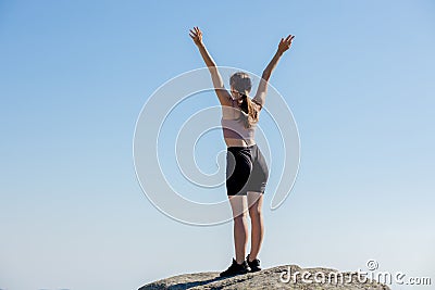 The young girl at the top of the mountain raised her hands up on blue sky background. The woman climbed to the top and enjoyed her Stock Photo