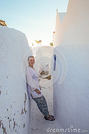 A young girl tourist in white clothes smiles and fills on the white walls of the city of Fira. Stock Photo