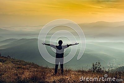 Young girl traveler stands on a cliff in the summer mountains at sunrise and enjoys a view of nature Stock Photo