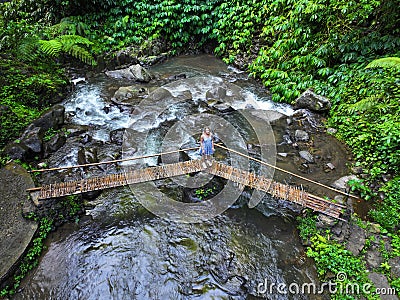 A young girl is walking on a small wooden bridge across the jungle stream Editorial Stock Photo