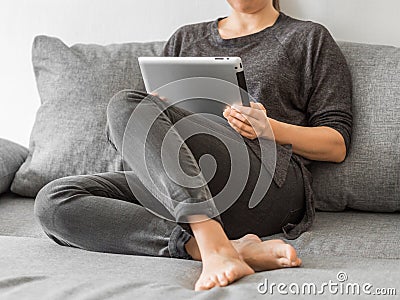 Young girl watching lessons on a tablet sitting on gray sofa. Business woman on quarantine. Online education concept Stock Photo