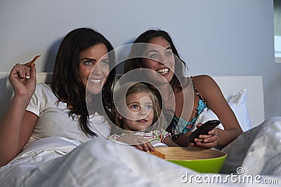 Young girl watching TV in bed with gay female parents Stock Photo