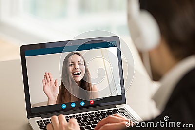 Young girl waving from laptop screen at man in headphones. Stock Photo