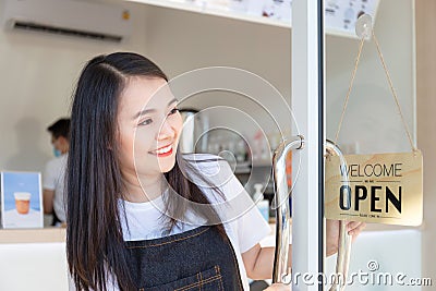 Young girl wearing an apron. Happy girl opening on the doors at a cafe and looking at open sign wood board Stock Photo
