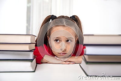 Shot of young girl sitting at the table with two large stacks of books and looking dreamily into the distance Stock Photo