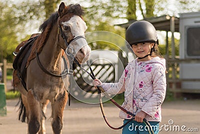 Young girl wearing riding helmet leading Welsh pony Stock Photo