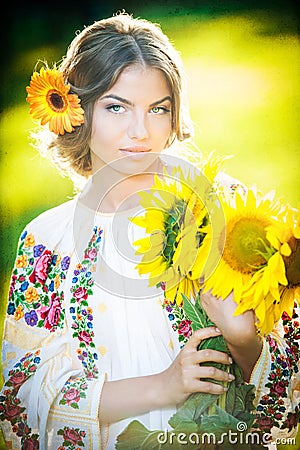 Young girl wearing Romanian traditional blouse holding sunflowers outdoor shot. Portrait of beautiful blonde girl with sunflowers Stock Photo