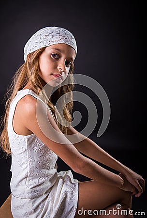 Young girl with white cap and sober look sitting on black background Stock Photo