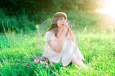 Young girl in white dress sitting in the middle of the field and reflects. Sadness, loneliness, doubt. Stock Photo