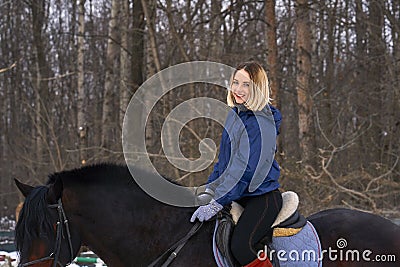 A young girl with white hair learns to ride a horse. The girl recently started to practice equestrianism. The girl is afraid of ri Stock Photo