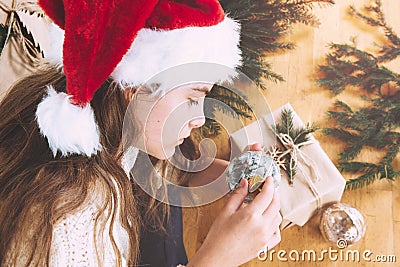 Young girl wraps present bouble christmas tree branches direct look santa hat Stock Photo