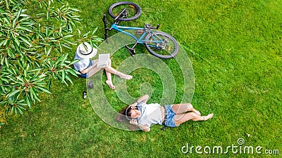 Young girls with bicycle in park, listening music with headphones and reading book, two student girls study and relax outdoors Stock Photo