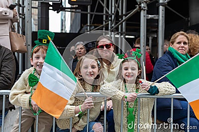 young girls at a parade wearing irish flags and glasses in front of a metal fence Editorial Stock Photo