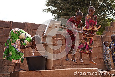 Young Girls Pumping Water At A Public Borehole in West Africa Stock Photo