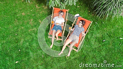 Young girls relax in summer garden in sunbed deckchairs on grass, women friends have fun outdoors in green park on weekend Stock Photo