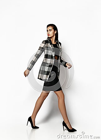 Young glamorous modern woman in hurry runs to work walking full body in checkered jacket with red lips Stock Photo