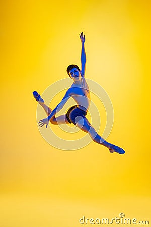 Young and graceful ballet dancer isolated on yellow studio background in neon light. Art, motion, action, flexibility Stock Photo