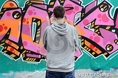 A young graffiti artist in a gray hoodie looks at the wall with Stock Photo