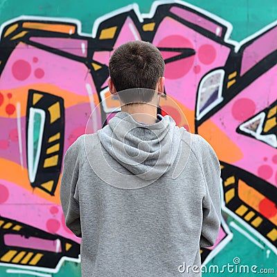 A young graffiti artist in a gray hoodie looks at the wall with Stock Photo