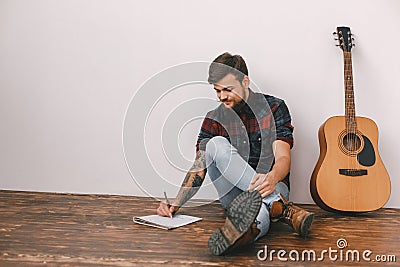 Young guitarist hipster at home with guitar sitting writing song Stock Photo