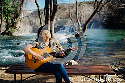 Young guitarist playing acoustic guitar and looking to river nature.Searching inspiration.Music creator.New artist in good mood. Stock Photo