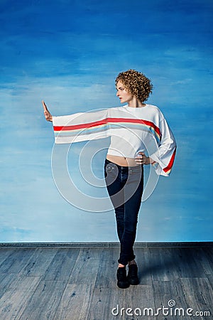 A young guy androgyne model in a white sweater with a rainbow symbol, stands on a blue background, looks in profile, Stock Photo