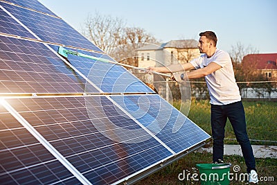 Young guy is cleaning solar panel on a plot near the house Stock Photo