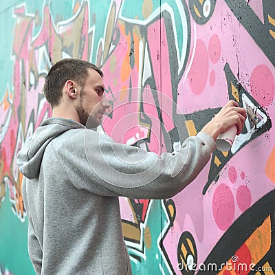 A young guy in a gray hoodie paints graffiti in pink and green c Stock Photo
